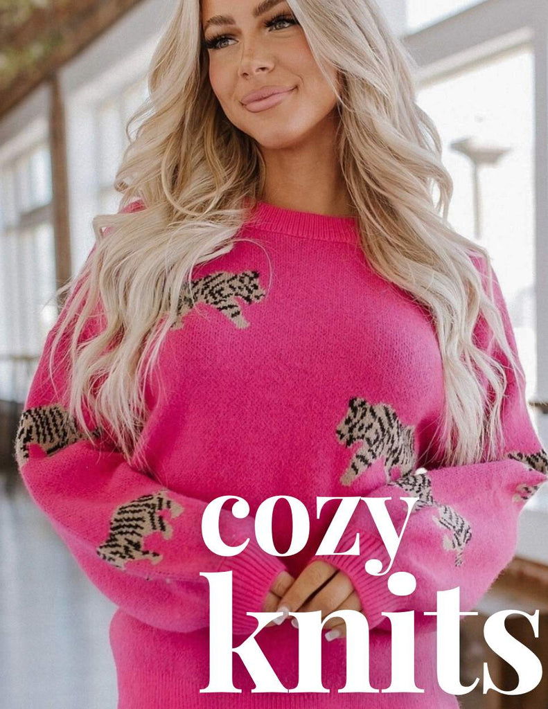 Bright pink oversized sweater with black and white leopard print design, featuring a relaxed fit and ribbed cuffs. Modeled by a woman with long blonde hair in a sunlit indoor setting. Stylish and cozy boho fashion from Oak&Pearl Clothing Co