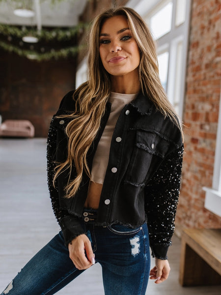 Black sequin sleeved jean jacket. Luxe combination of black sequins and denim. Button up, front pockets with frayed detail.