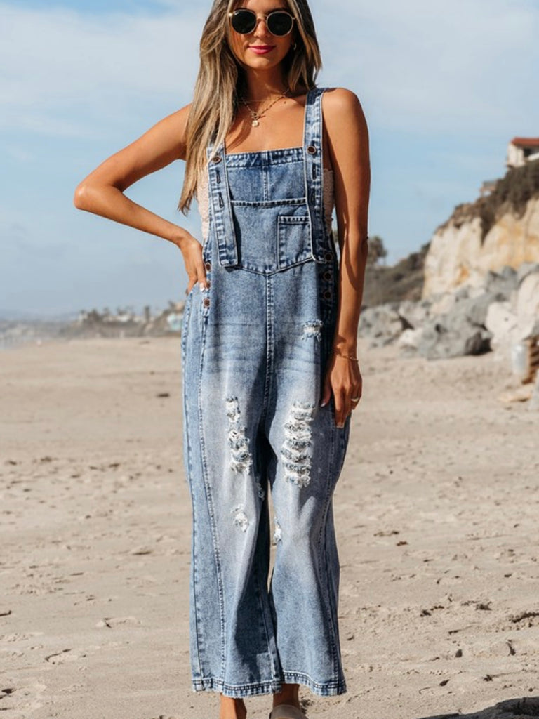 Blonde woman wearing wide leg distressed denim overalls on the beach