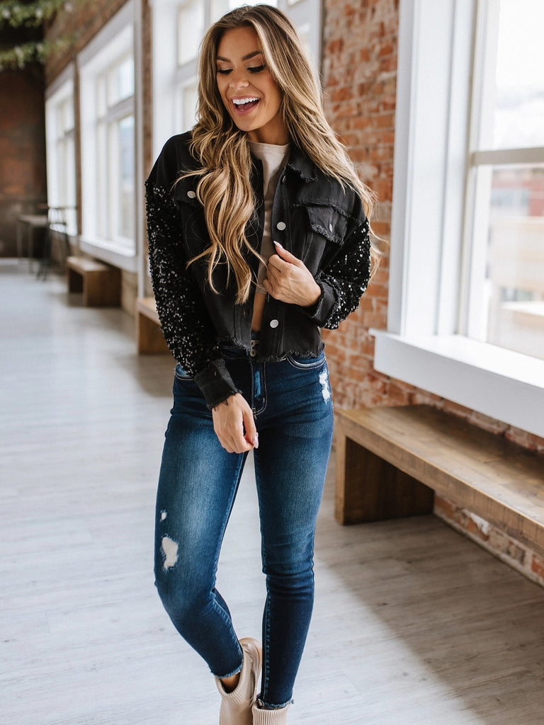 Black sequin sleeved jean jacket. Luxe combination of black sequins and denim. Button up, front pockets with frayed detail.