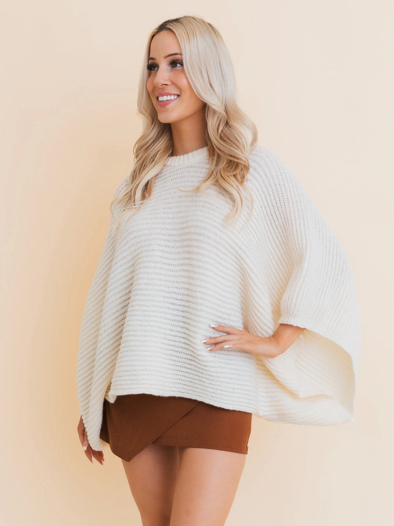 Metro Poncho. Premium ribbed knit and stylish bell sleeves, this versatile poncho is perfect for any occasion. Available in Black or Ivory, elevate your cozy season wardrobe with this must-have essential. 100% Polyester.