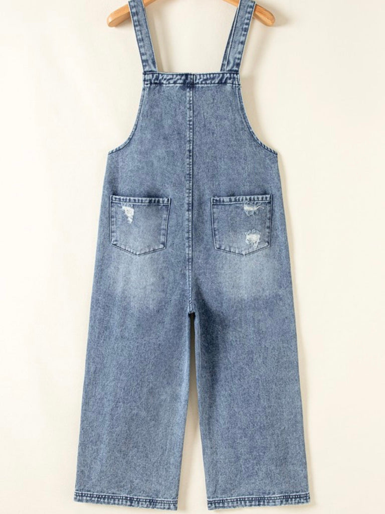 Back view of blue denim overalls laid flat with strap details