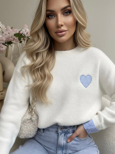 Woman wearing a white sweater with a blue plaid heart design.