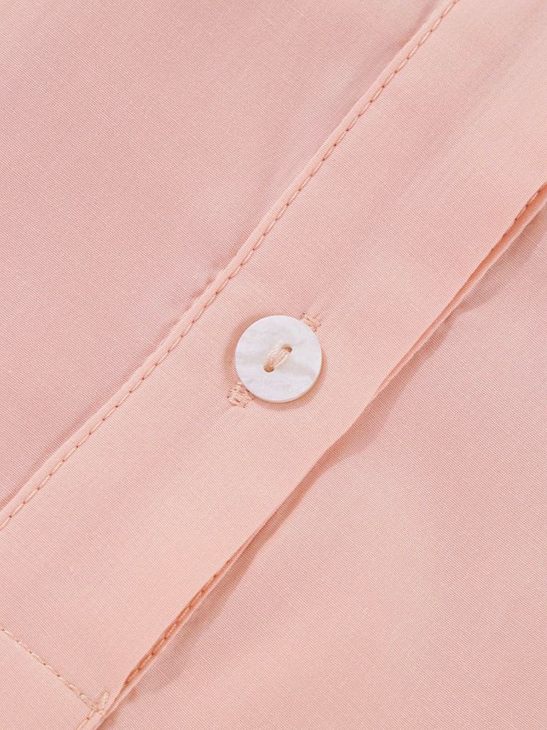Close-up view of white button and placket stitching on pink shirt dress