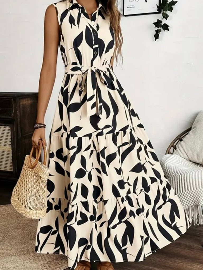 Woman wearing a belted sleeveless maxi dress with bold black and beige print and tiered design.