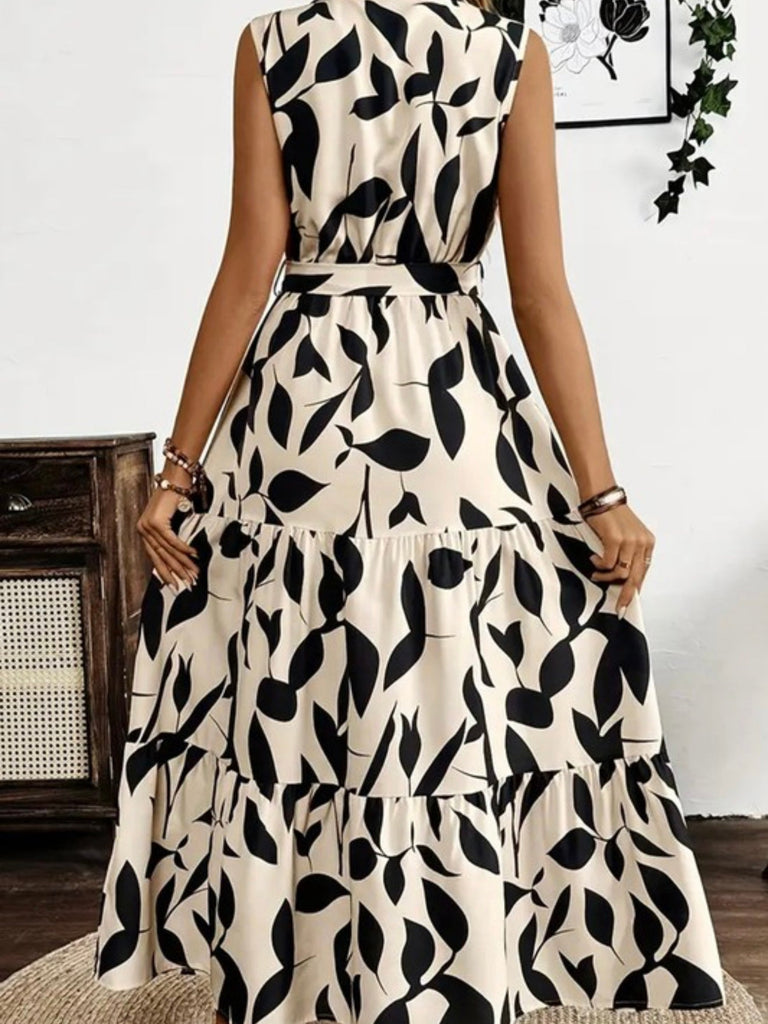 Model walking in a sleeveless printed maxi dress with flowy tiered hem and neutral abstract pattern.