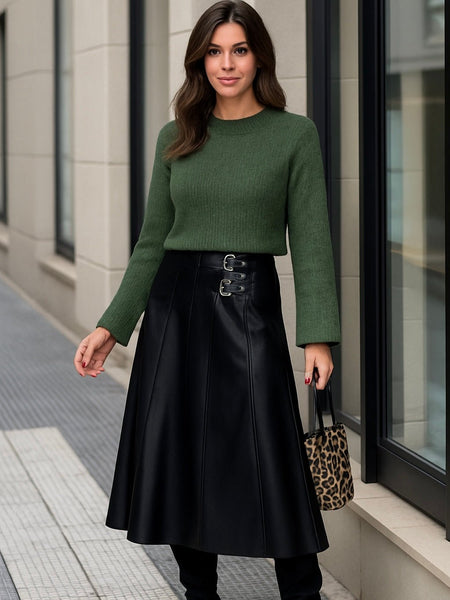Woman wearing a green sweater and black faux leather buckle waist skirt.