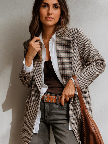 Woman wearing a plaid blazer over a white shirt, holding a brown leather bag.