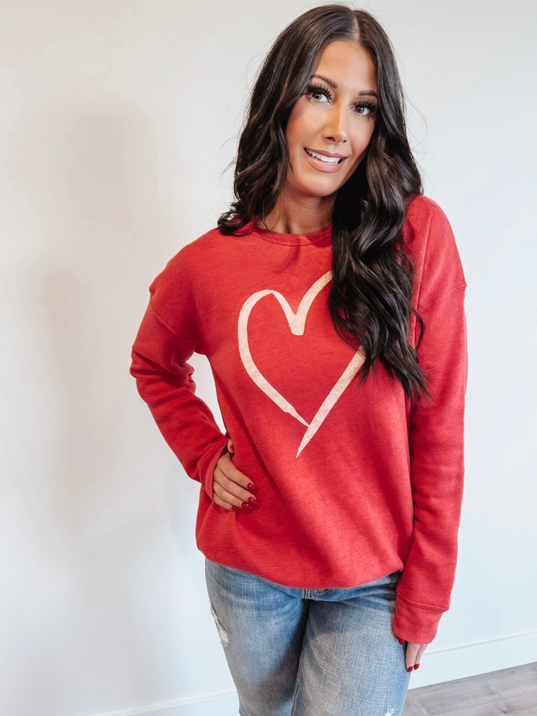 A woman wearing a red heart sweatshirt with a white heart graphic on the front.