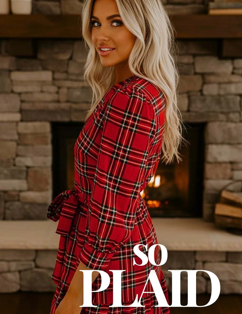 Woman wearing red plaid dress standing by a stone fireplace – Oak & Pearl Clothing Co.
