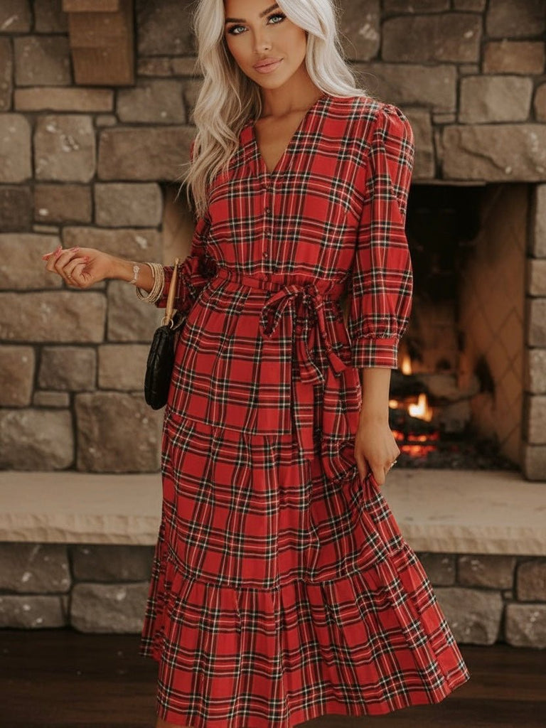 Woman wearing a festive red plaid dress standing in front of a stone fireplace.