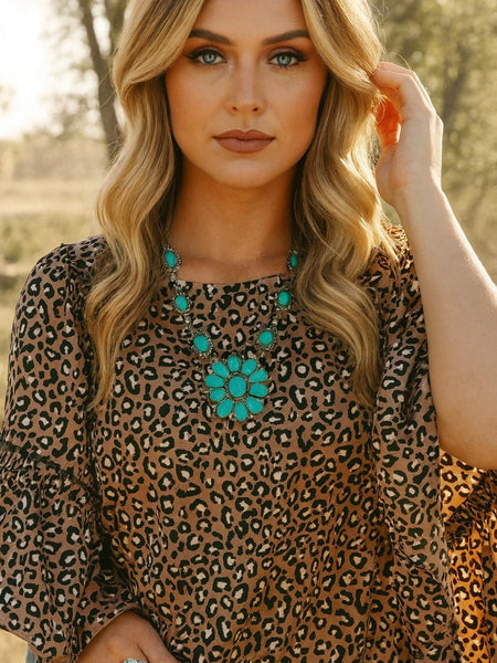 Woman wearing a leopard print top with bell sleeves and turquoise jewelry.
