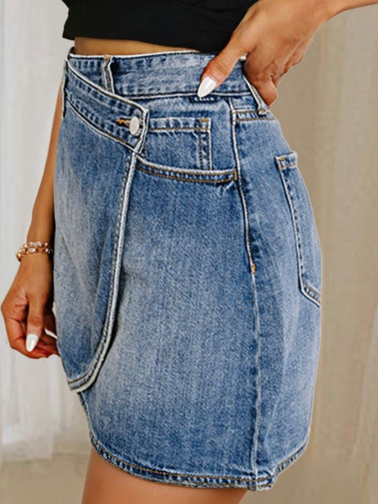 Side view of a blue denim mini skirt with asymmetrical wrap-style hem and button detail.